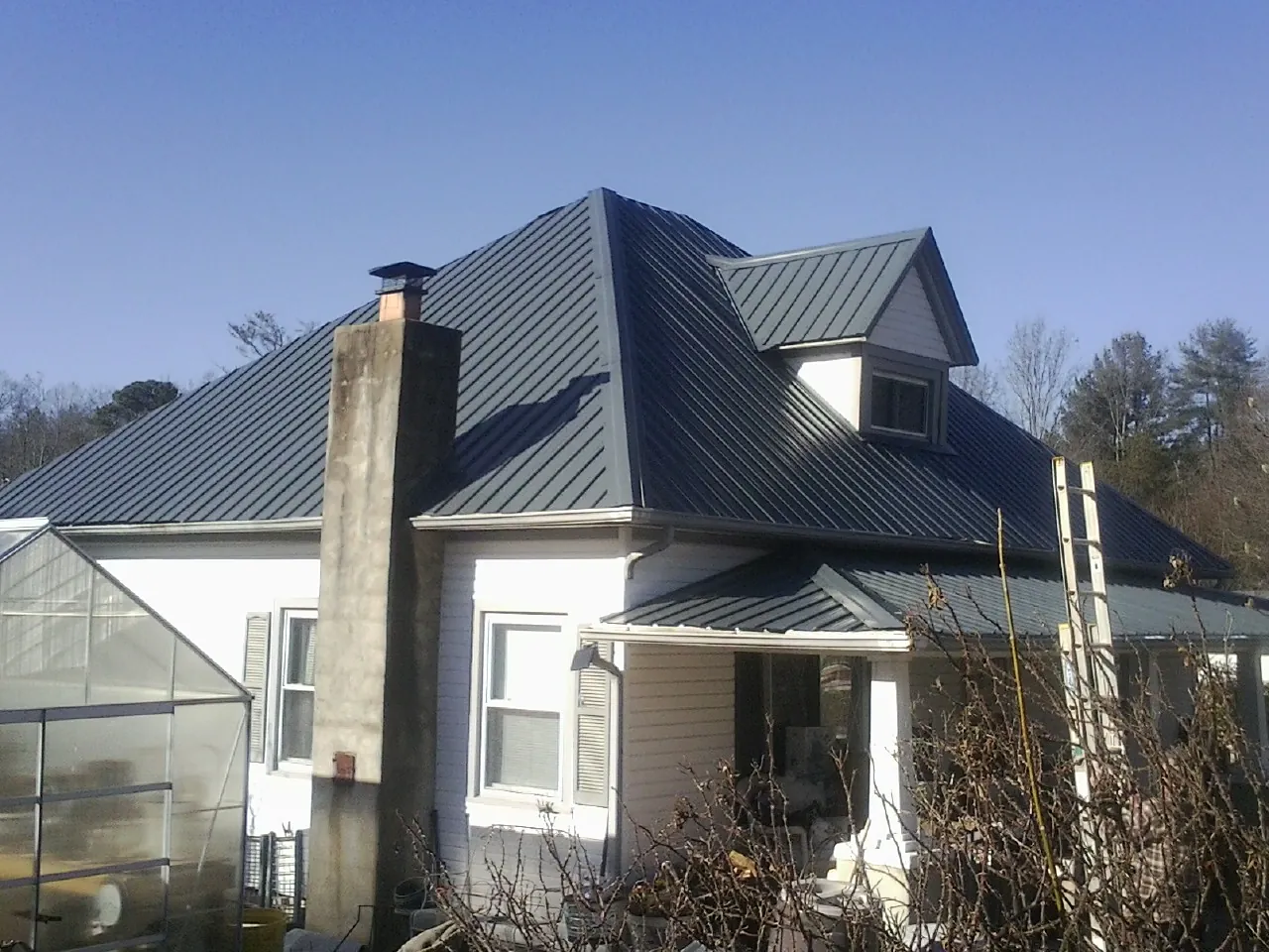 Dark blue standing seam metal roof on a white farmhouse with dormer — Slate & Tile Roof Repair by Roofing Brothers in Rosedale