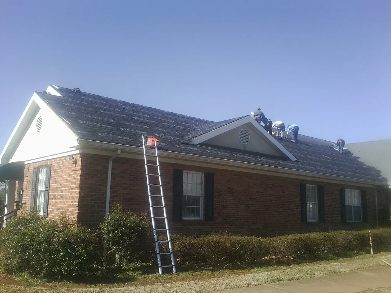 Crew tearing shingles off a brick ranch roof with a ladder set — Metal Roof Repair work by our crew in Rosedale