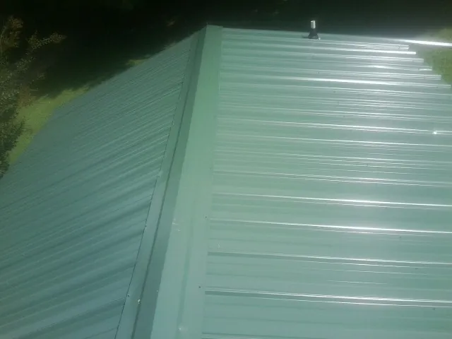 New green metal panels meeting at the ridge of a roof — Flat Roof Repair work by our crew in Rosedale