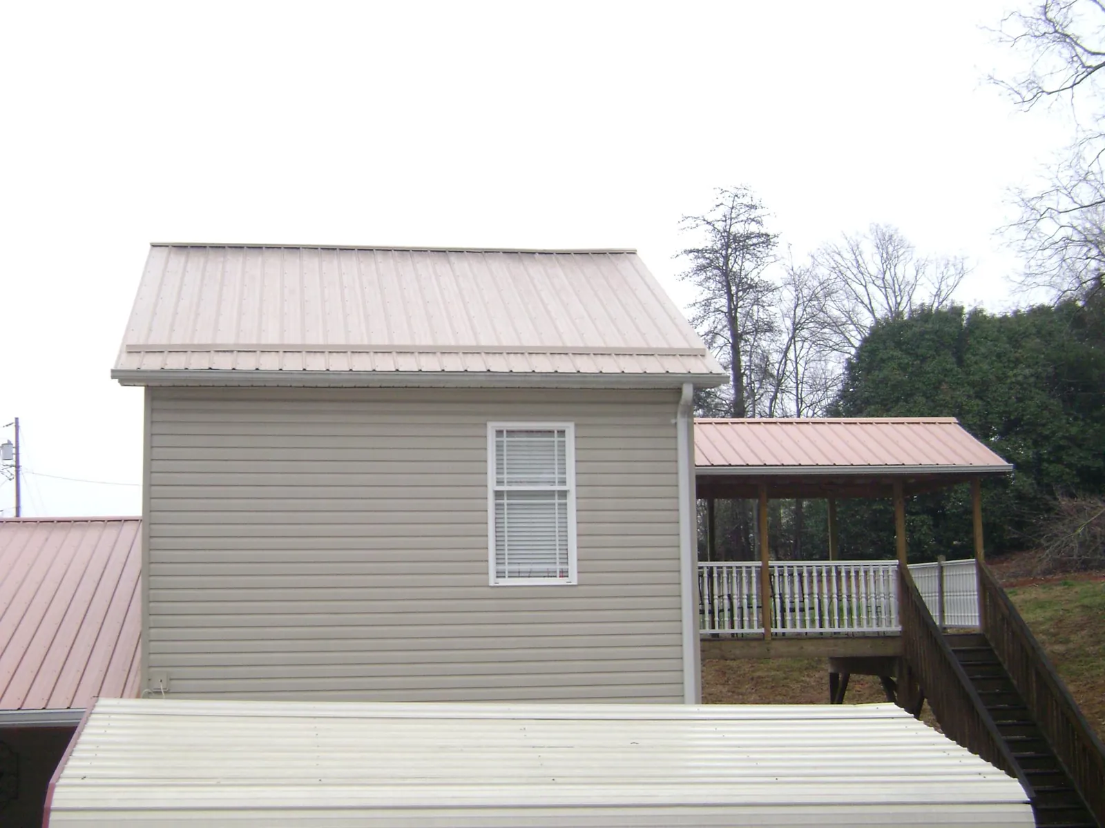 Tan metal roofs on a two story addition and attached porch, from a Roof Replacement job in Rosedale